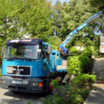 Das Foto zeigt Kranarbeit, bei der ein Lkw mit Kranarm eine Baumaschine über eine Treppe anhebt. Eser in Augsburg bietet Spezialkrantransporte an und stellt verschiedene Kranservices zum Mieten bereit.