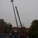 Das Foto zeigt Kranarbeit, bei der ein Lkw mit Kranarm einen Maibaum in großer Höhe aufstellt. Eser in Augsburg bietet Spezialkrantransporte an und stellt verschiedene Kranservices zum Mieten bereit.
